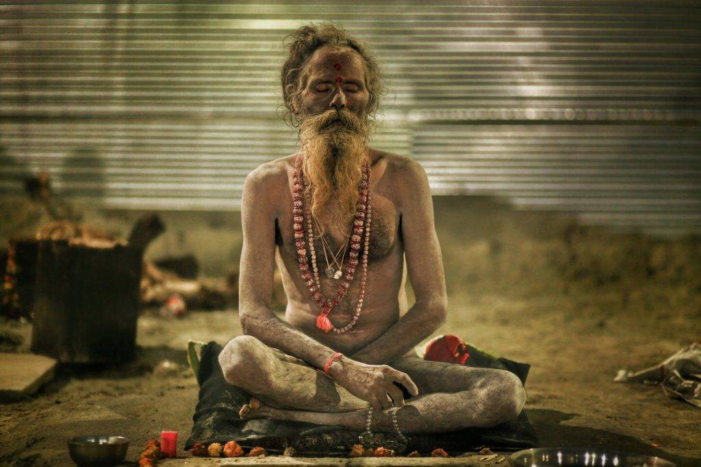 aghori sadhu meditating in sitting posture with garland beads in hands